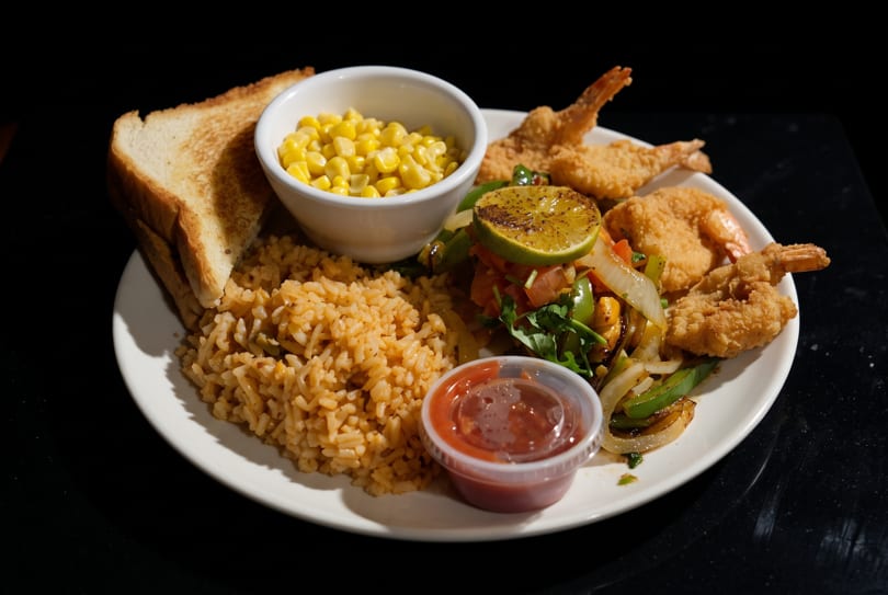 Fried shrimp, rice, corn, grilled vegetables, toast, and salsa on a white plate.