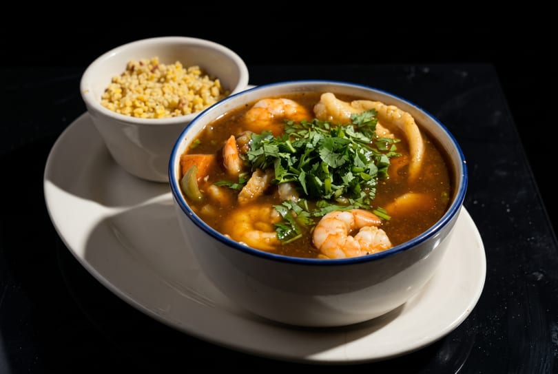 Shrimp and vegetable stew with cilantro in a white bowl, served with a side of rice.